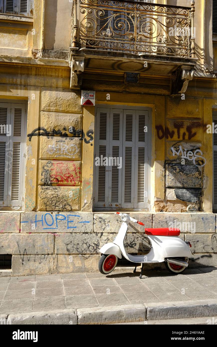 Uno scooter rosso e bianco parcheggiato di fronte ad un edificio con graffiti ad Atene, in Grecia Foto Stock