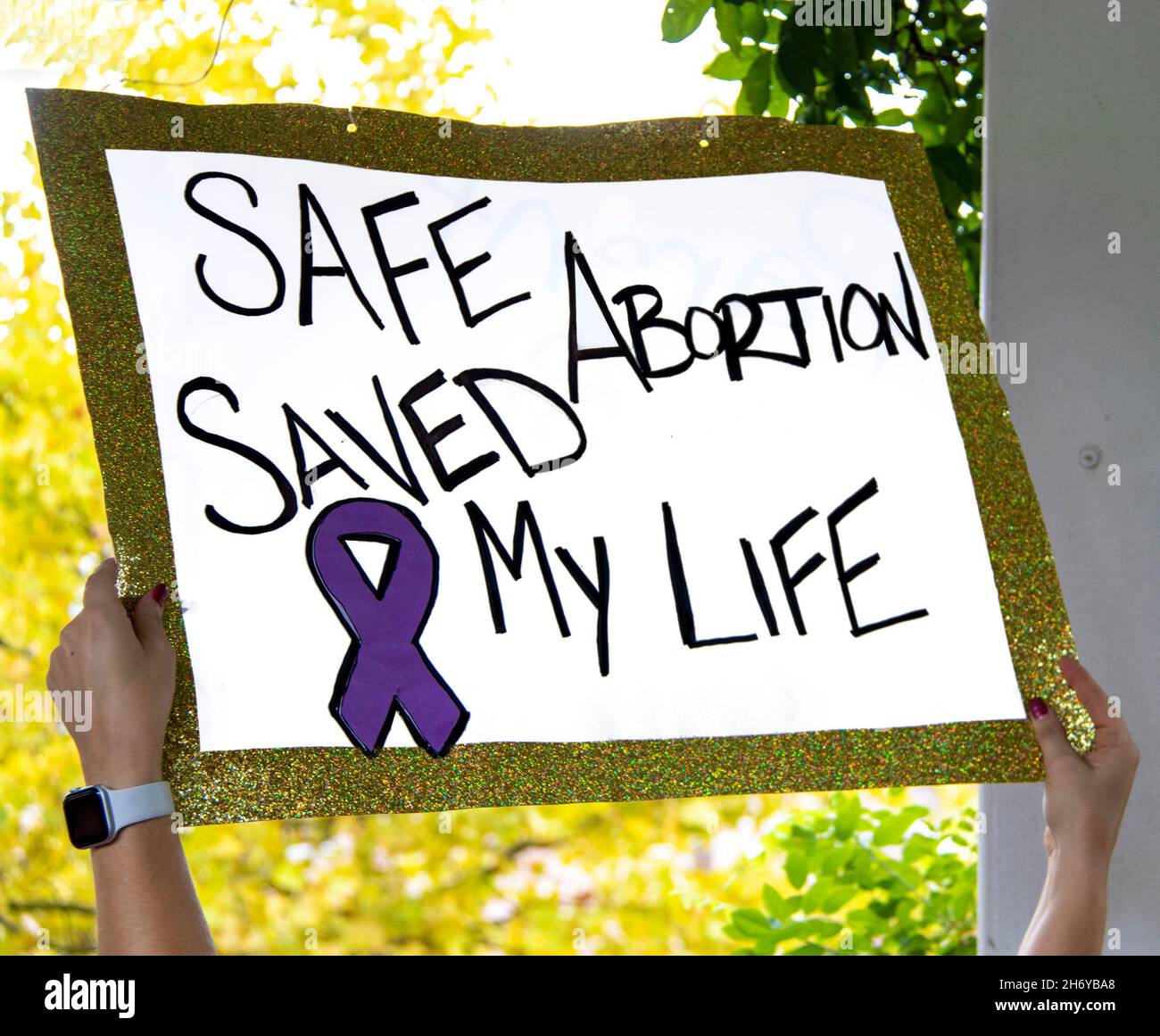 Sign with glitter edge reads Safe abortion Saved My Live - Blurred outdoor background at Reproductive Justice Rally Foto Stock