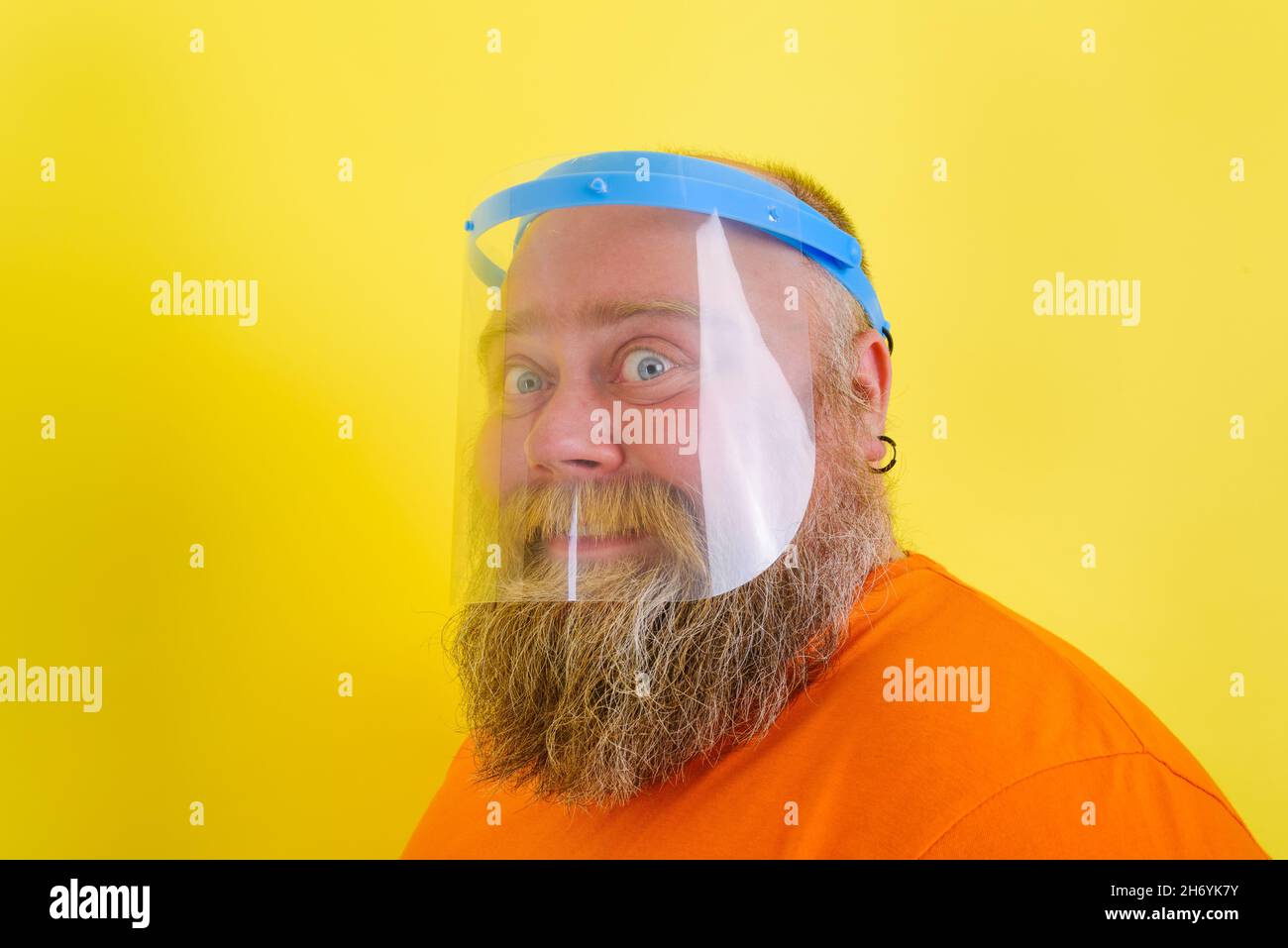 L'uomo felice con barba e tatuaggi indossa uno scudo protettivo contro il covid-19 Foto Stock
