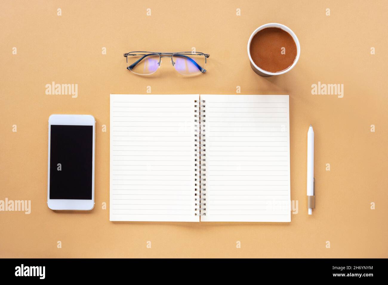 Blocco note vuoto, penna, caffè in una tazza di carta, smartphone e bicchieri su tavolo beige. Vista dall'alto, piatto, mock up. Foto Stock