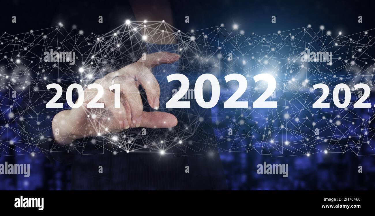 Concetto di nuovo anno. Mano Hold digitale ologramma 2022 segno sulla città scuro sfondo sfocato. Felice anno nuovo 2022. Concetto di visione 2021-2022. Uomo d'affari Foto Stock