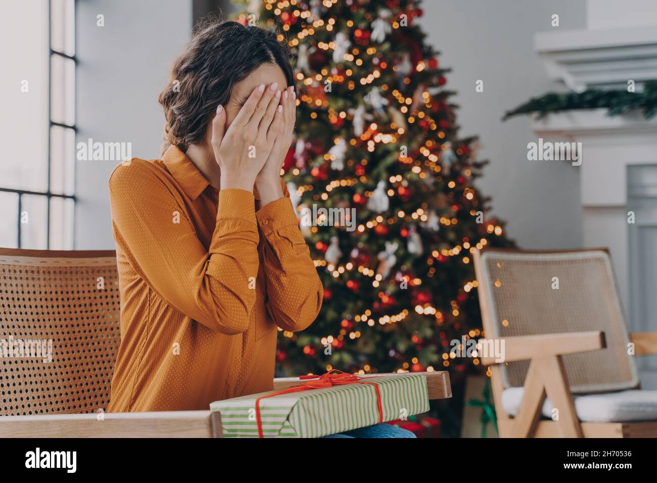 Donna curiosa che copre gli occhi con le mani e indovinare che cosa all'interno della scatola del regalo di Natale Foto Stock