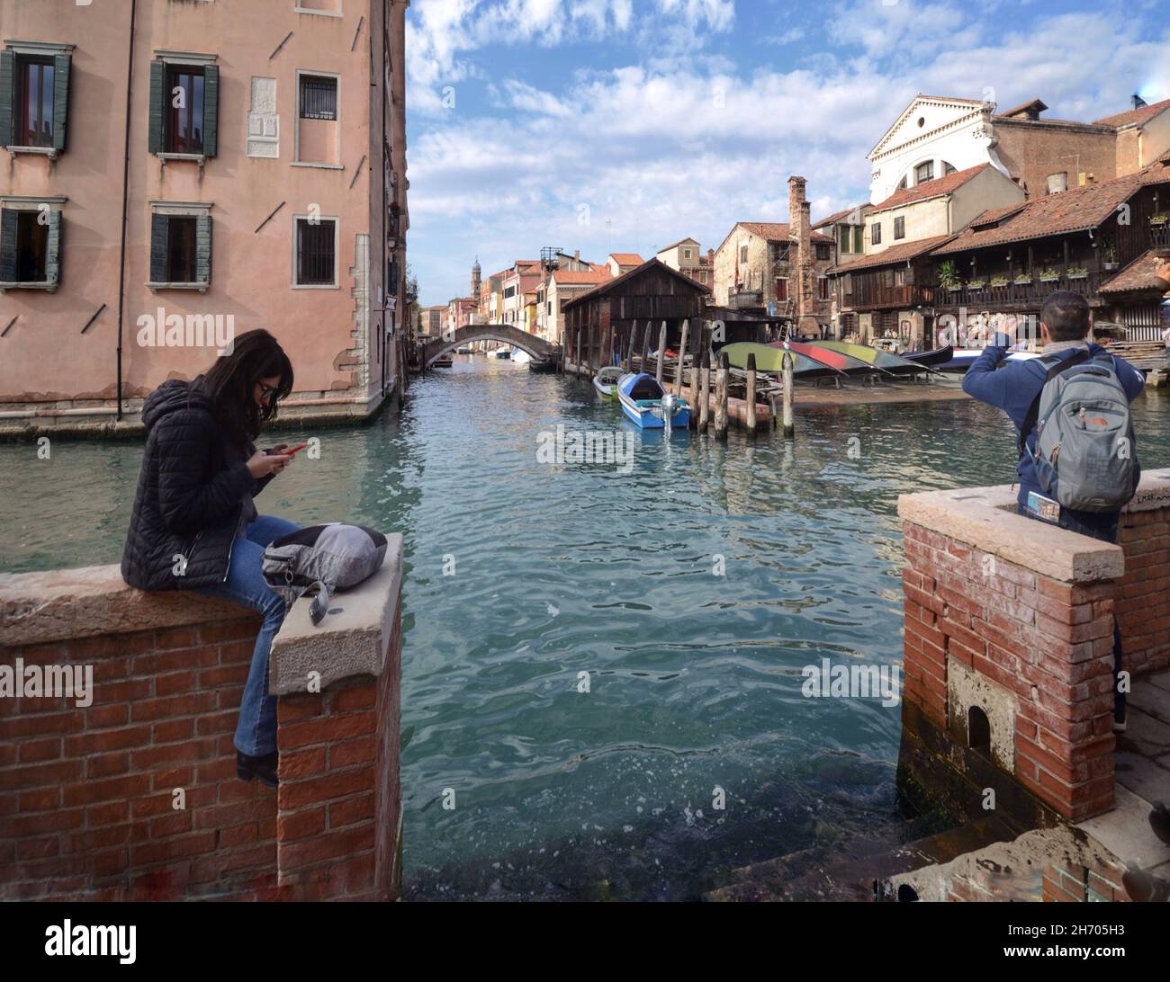 Ragazza e ragazzo lungo un canale di Venezia usano il loro smartphone Foto Stock