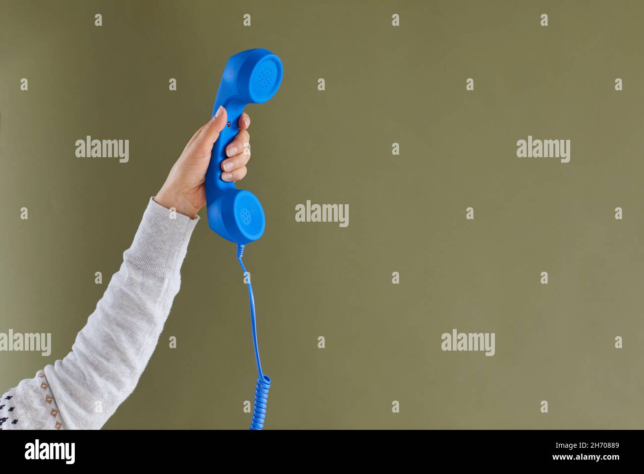 Primo piano di una mano donna che tiene il telefono cellulare con filo blu su sfondo verde. Foto Stock