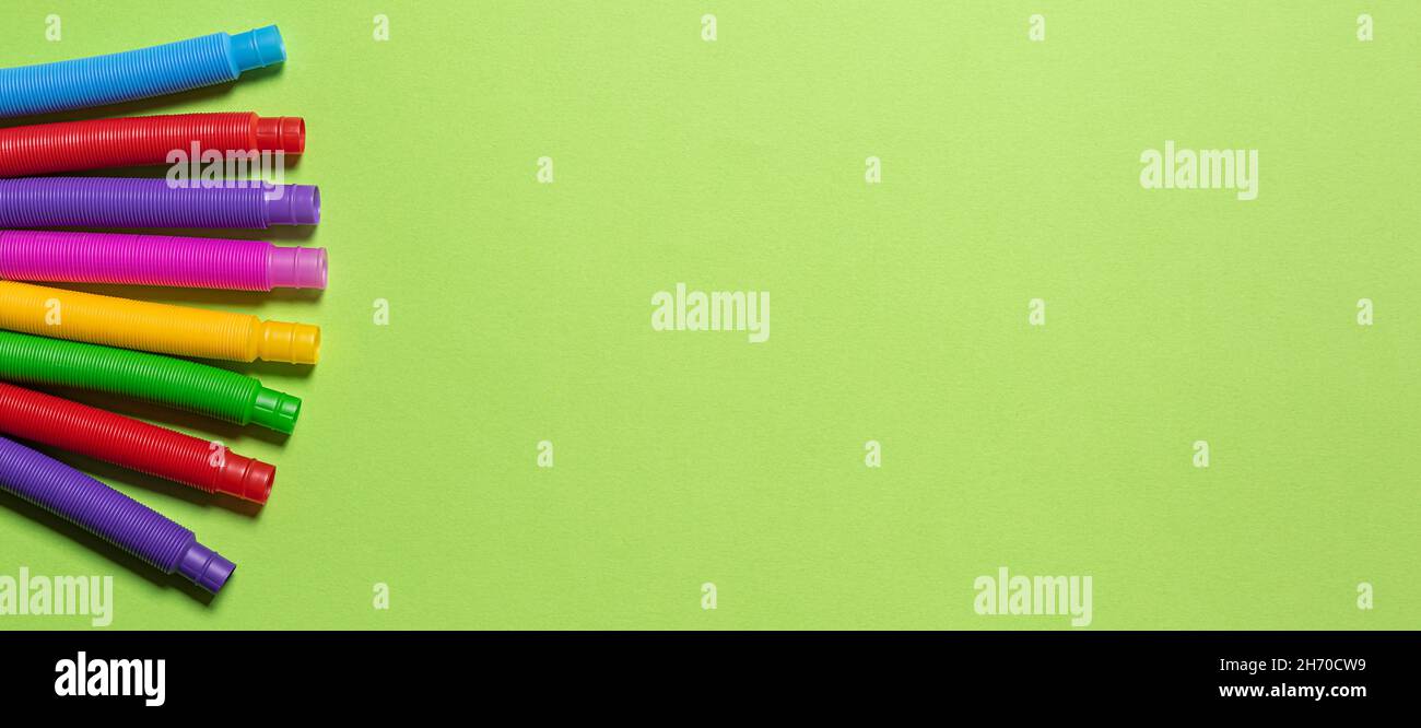 Banner con gruppo di giocattoli multicolori per bambini con tubo anti-stress rosso, blu, rosa, verde e giallo. Disposizione piatta con set di tubi colorati in plastica su Foto Stock