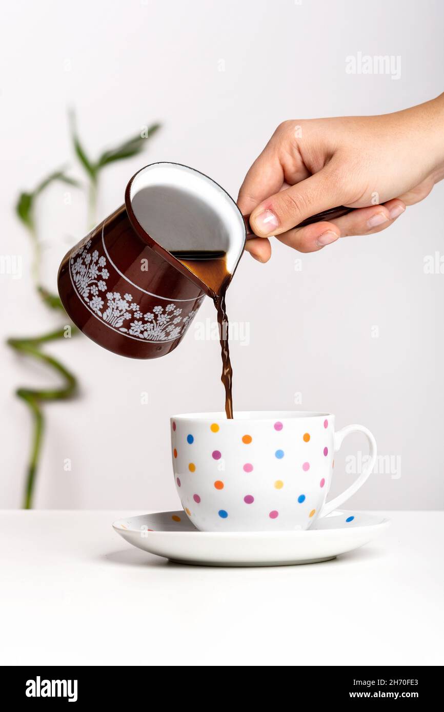Versare il caffè nero turco appena fatto in una tazza da una cezve. Foto Stock