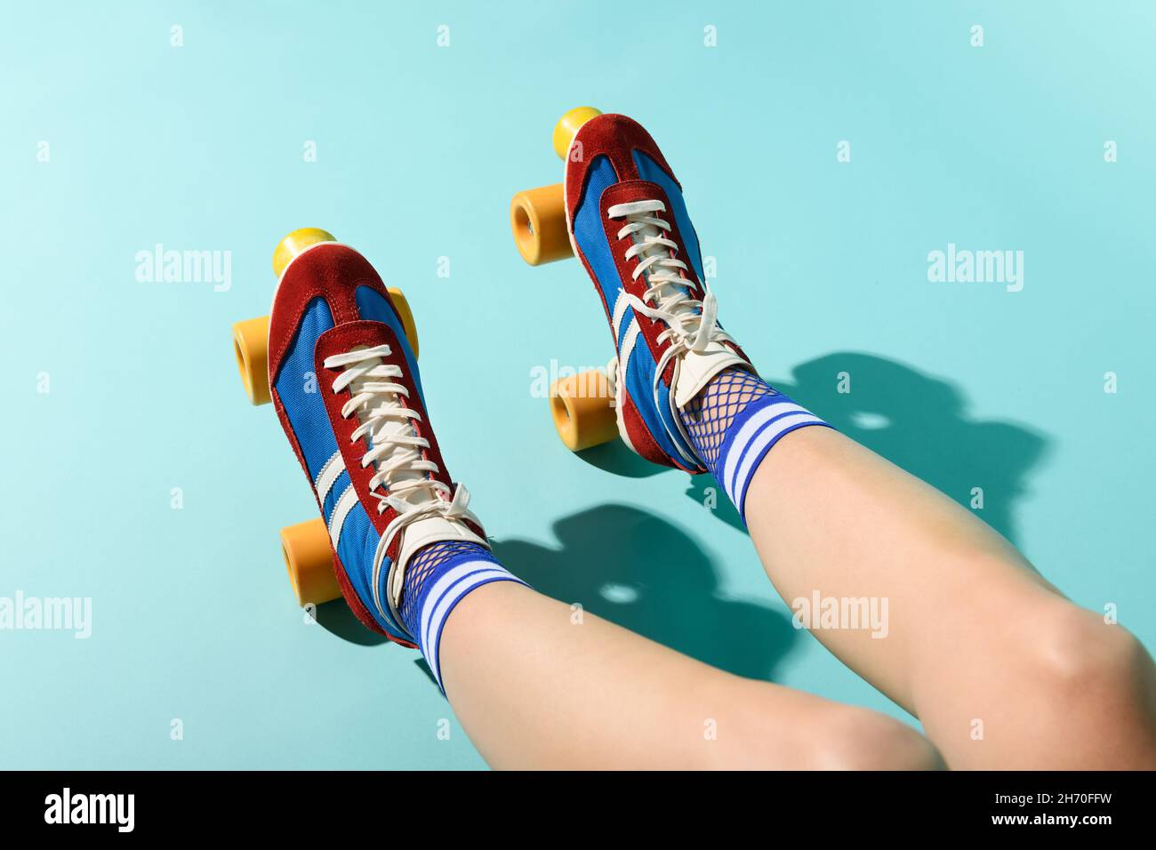 Da sopra di raccolto anonima femmina in calze colorate e luminose pattini a rotelle che riposano alla luce del sole su sfondo blu Foto Stock