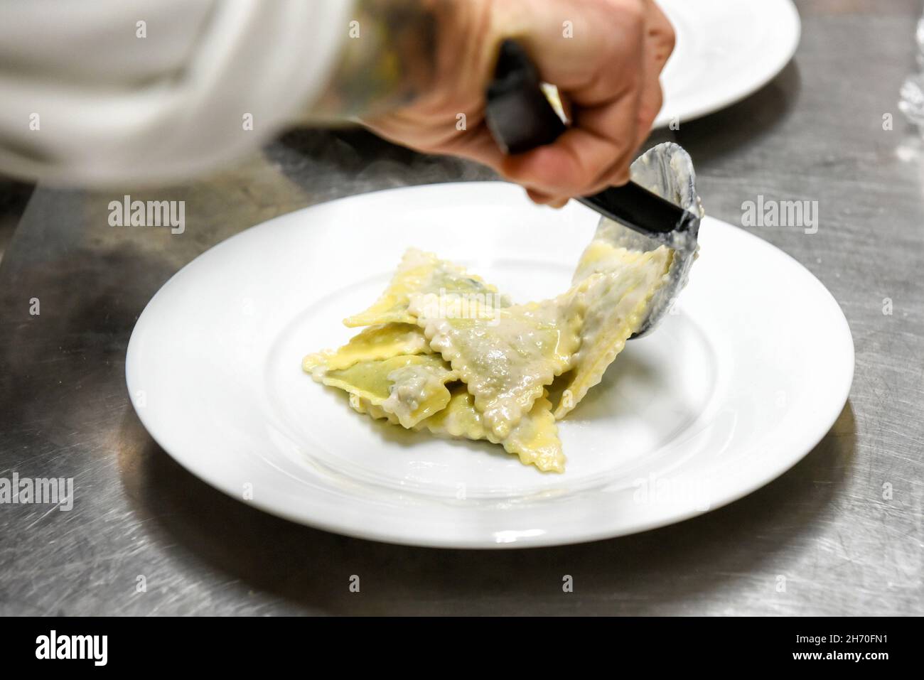 Coltivare il cuoco anonimo con cucchiaio da cucina mettendo appetitosi ravioli tradizionali italiani su piatto bianco mentre si serve il pasto al ristorante Foto Stock