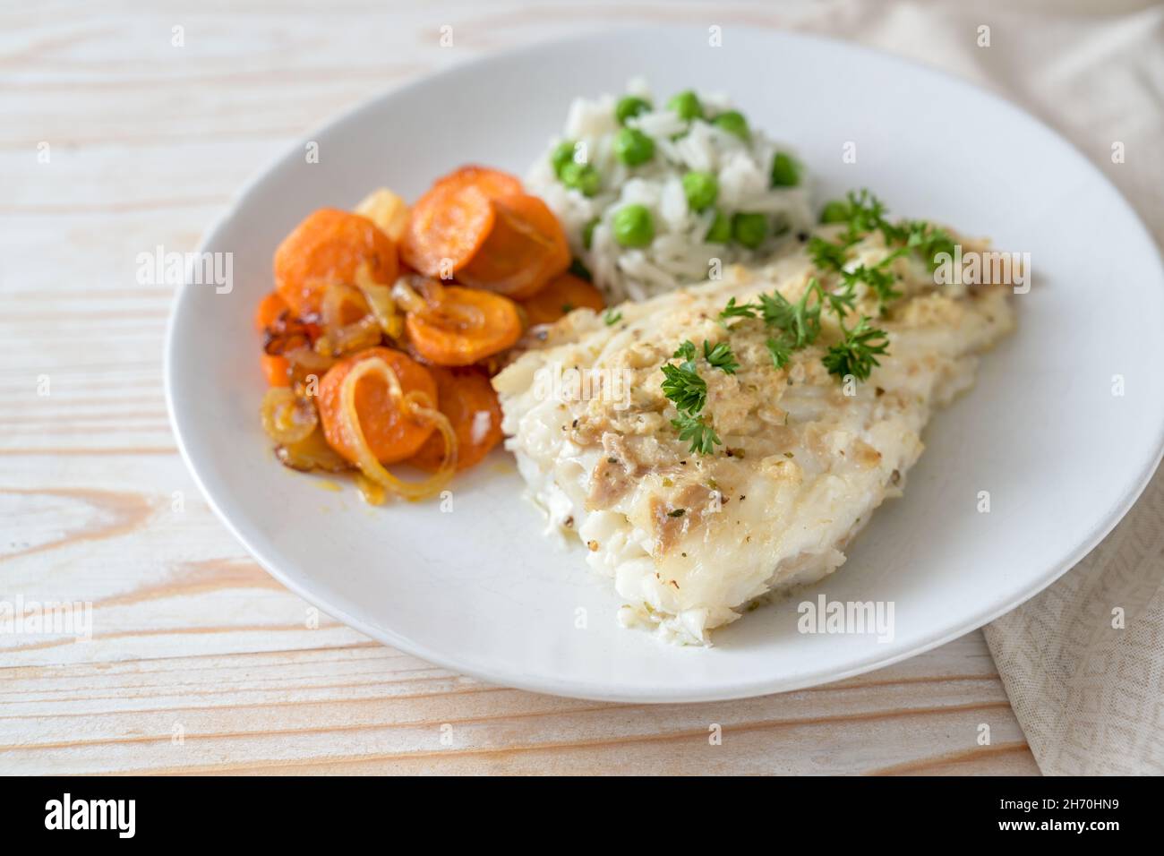 Filetto di merluzzo con contorno di prezzemolo, carote e riso al pisello verde su un piatto bianco, pasto di pesce sano, fuoco selezionato, profondità di campo molto stretta Foto Stock