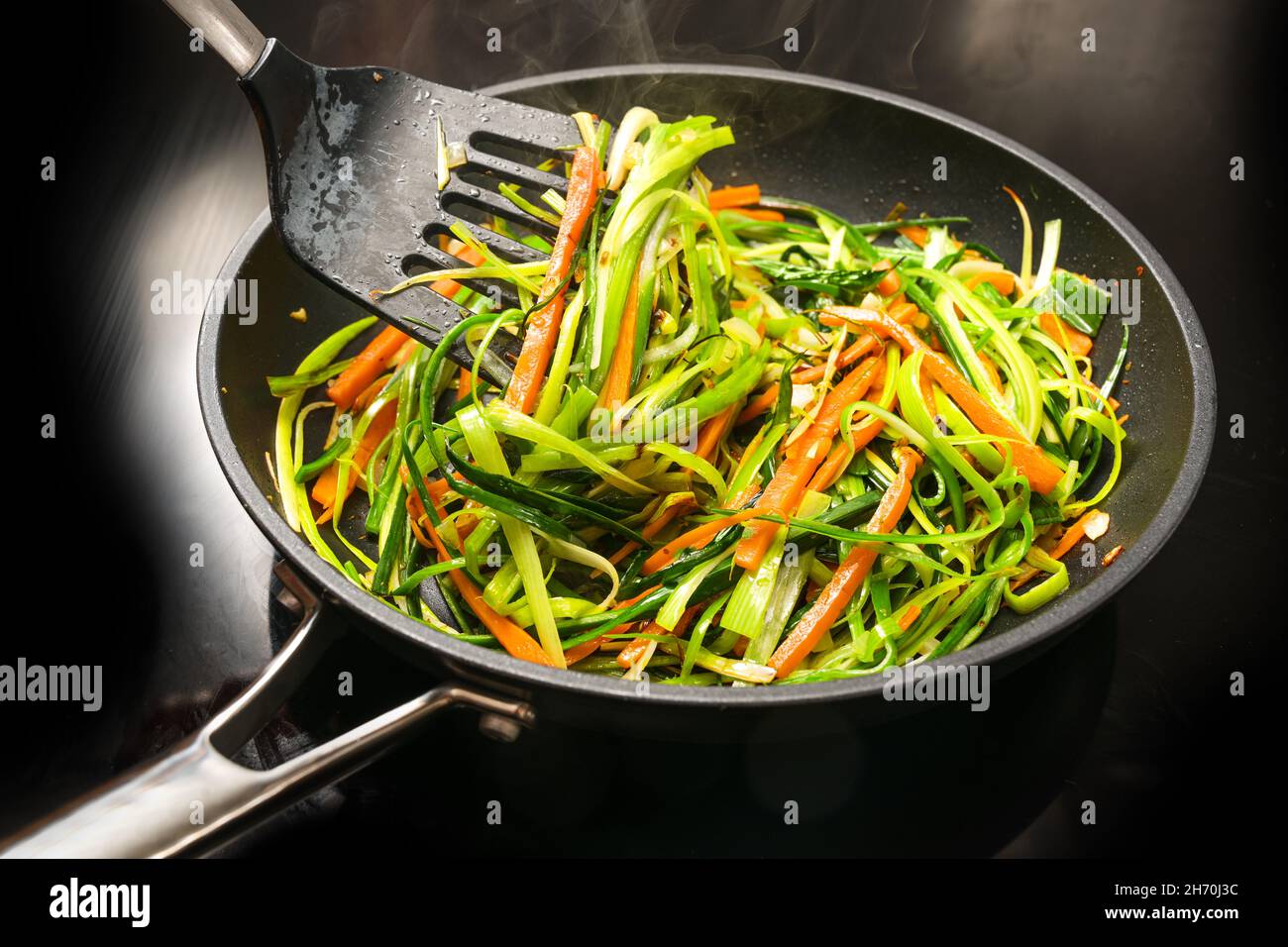 Cottura di tagliatelle di verdure sane da julienne di carota e strisce di porri verdi in una padella nera, per un pasto vegetariano, fuoco selezionato, dept stretto Foto Stock