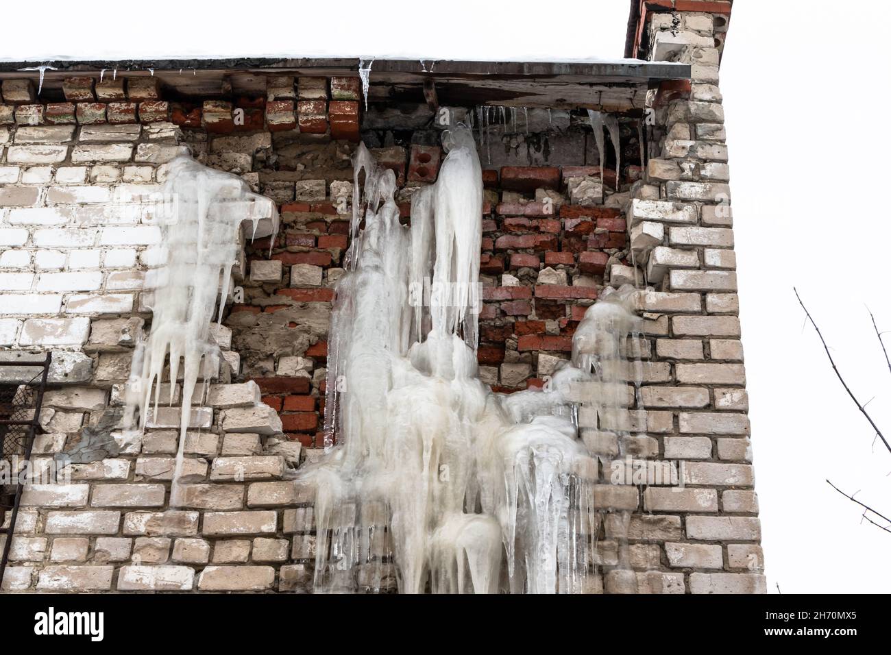 Un vecchio muro distrutto di un edificio bianco di mattoni con ghiaccioli in una gelida giornata invernale contro un cielo grigio e cupo. Messa a fuoco selettiva. Primo piano Foto Stock