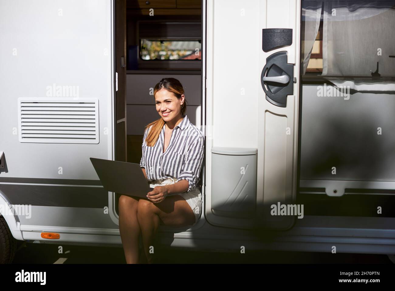 Donna seduta alla porta caravan e utilizzando un computer portatile Foto Stock