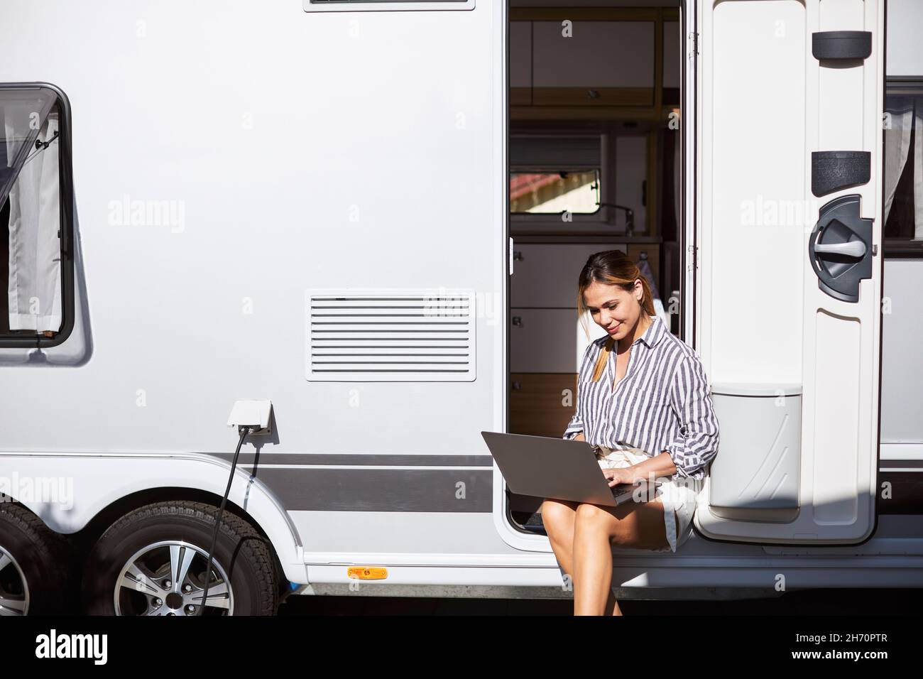 Donna seduta alla porta caravan e utilizzando un computer portatile Foto Stock