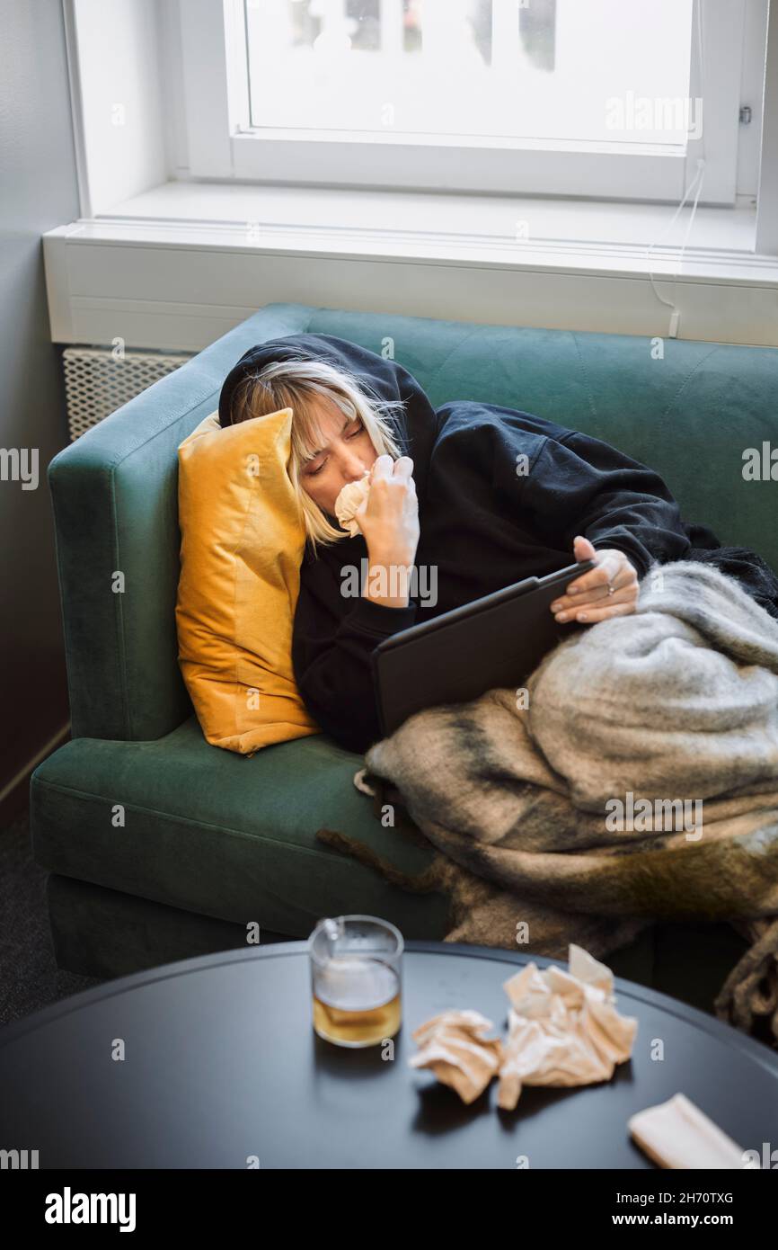 Donna malata sul divano con tablet digitale Foto Stock
