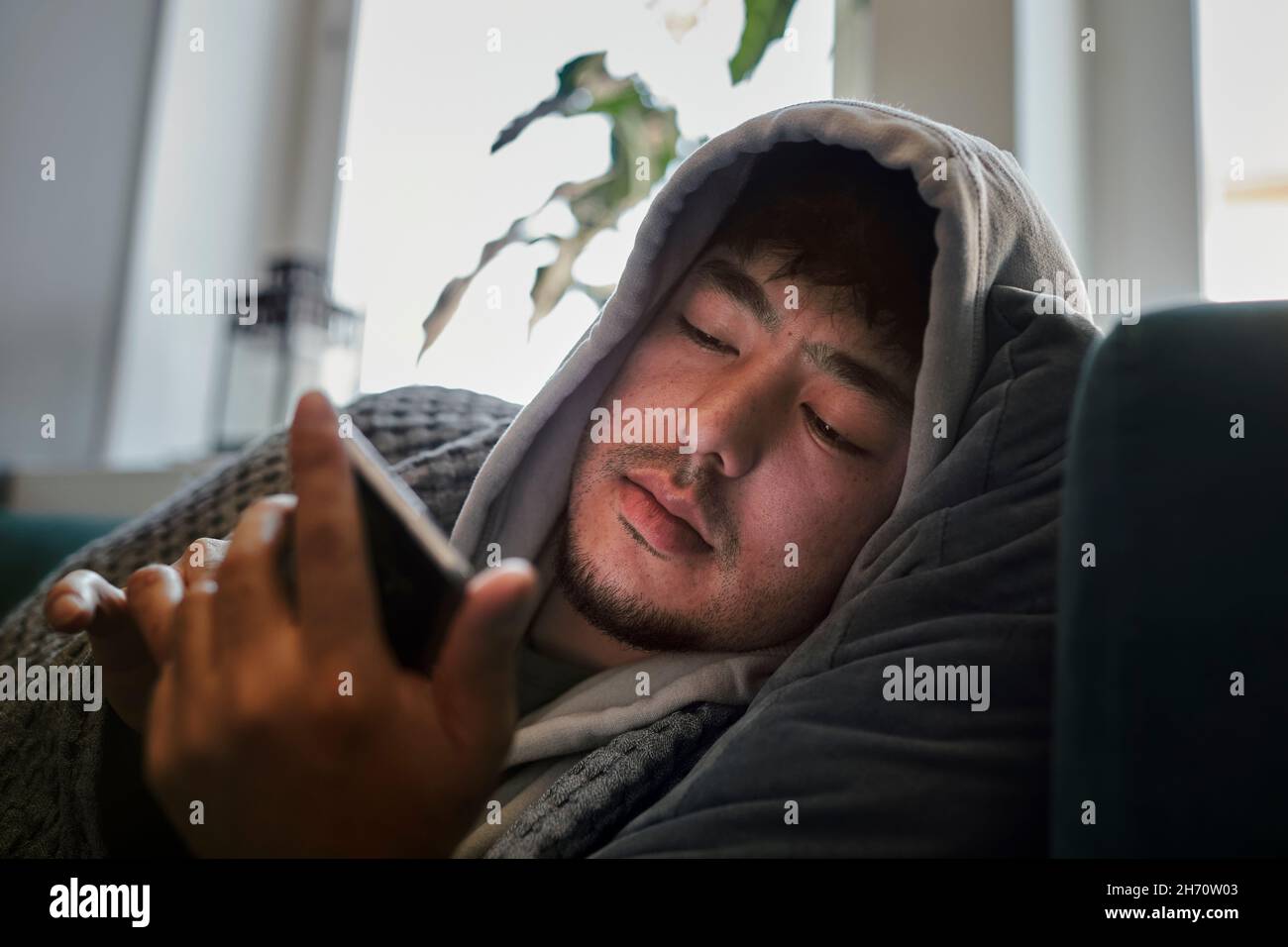 Uomo malato sul divano usando il telefono cellulare Foto Stock