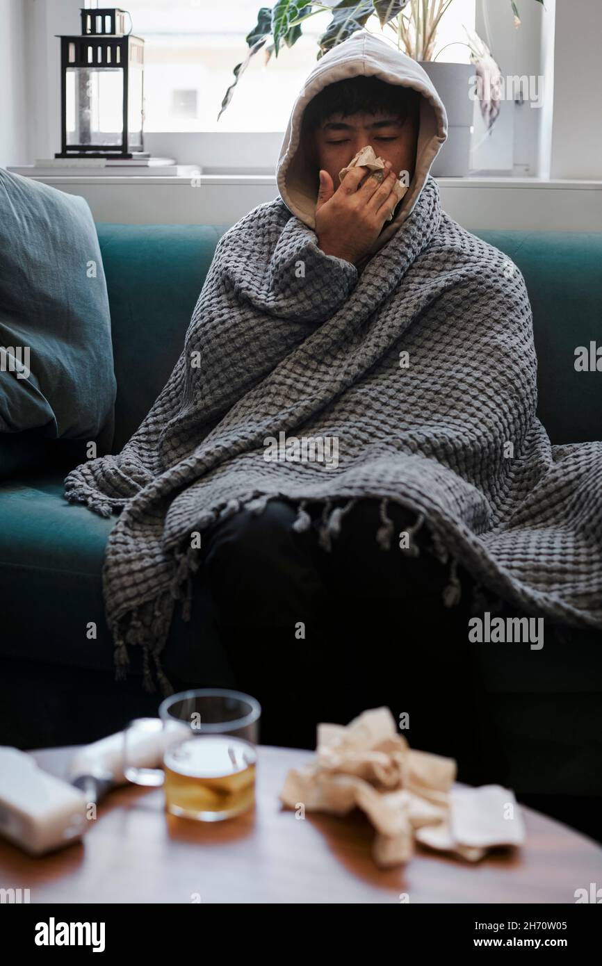 L'uomo malato sul divano soffia il naso Foto Stock