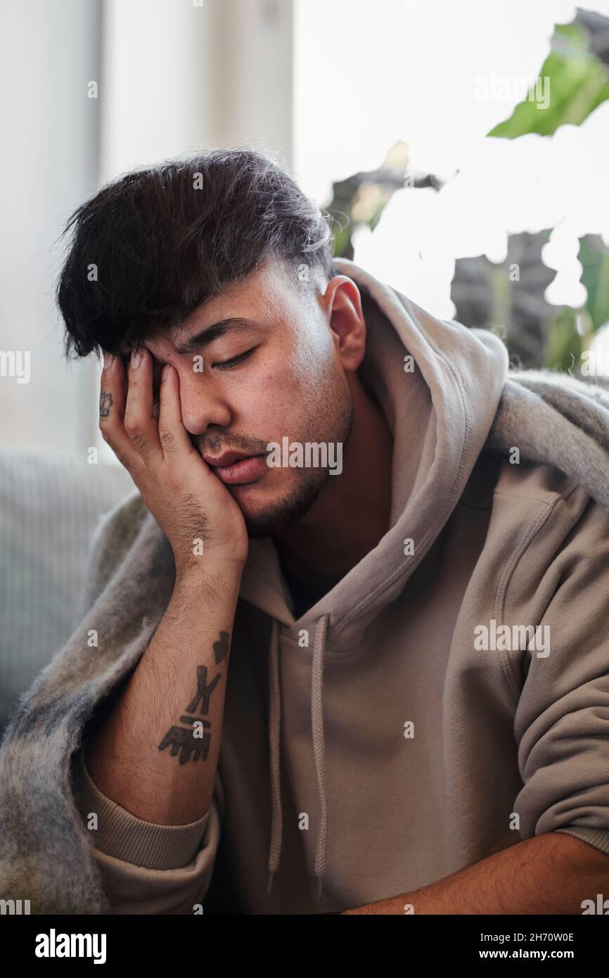 Uomo malato sul divano con la mano che copre il viso Foto Stock