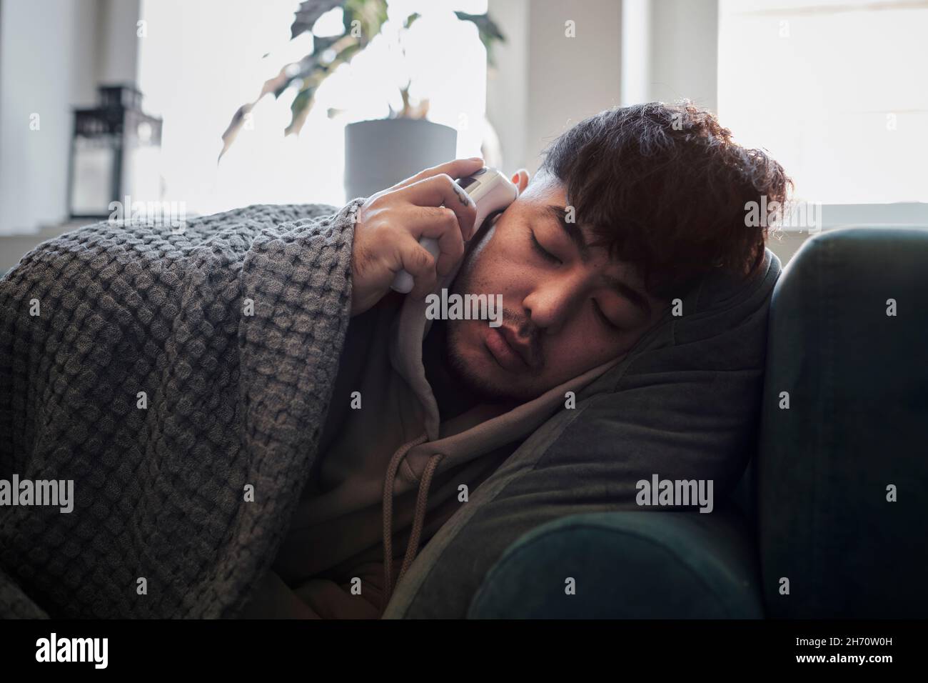 Uomo malato sul divano controllo della temperatura Foto Stock