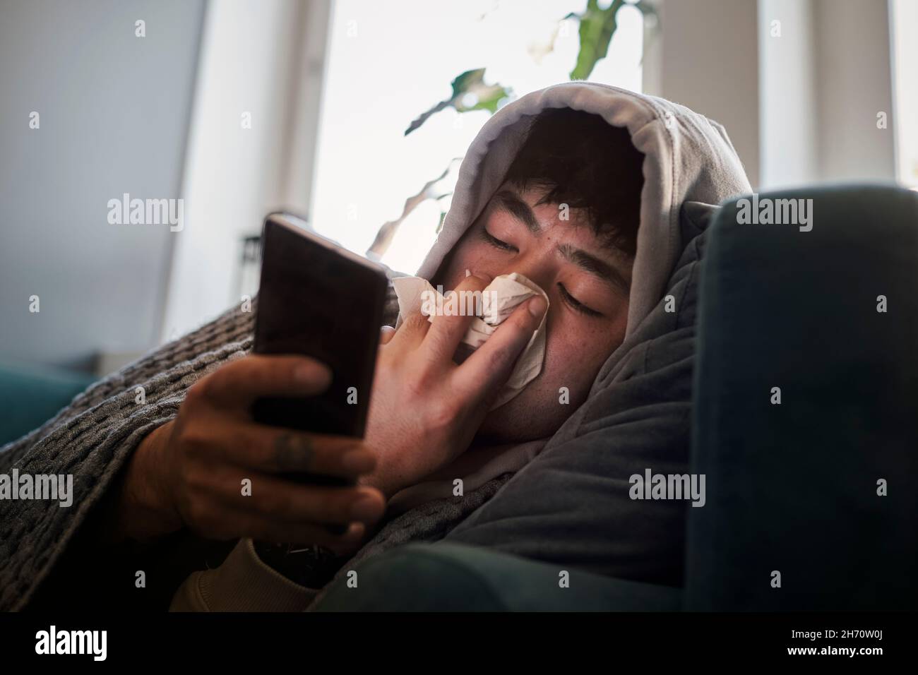 Uomo malato sul divano usando il telefono cellulare Foto Stock