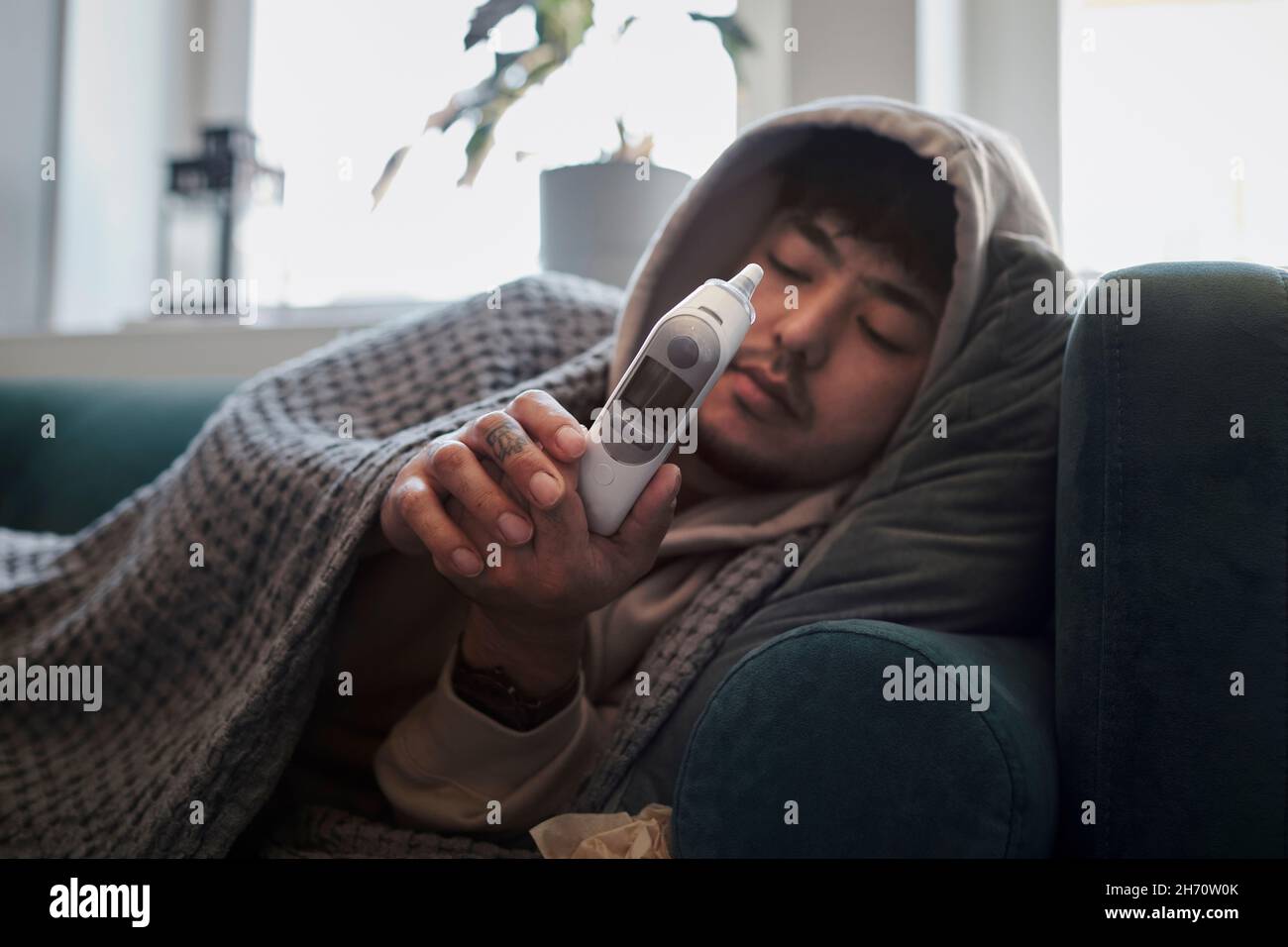 Uomo malato sul divano controllo termometro Foto Stock