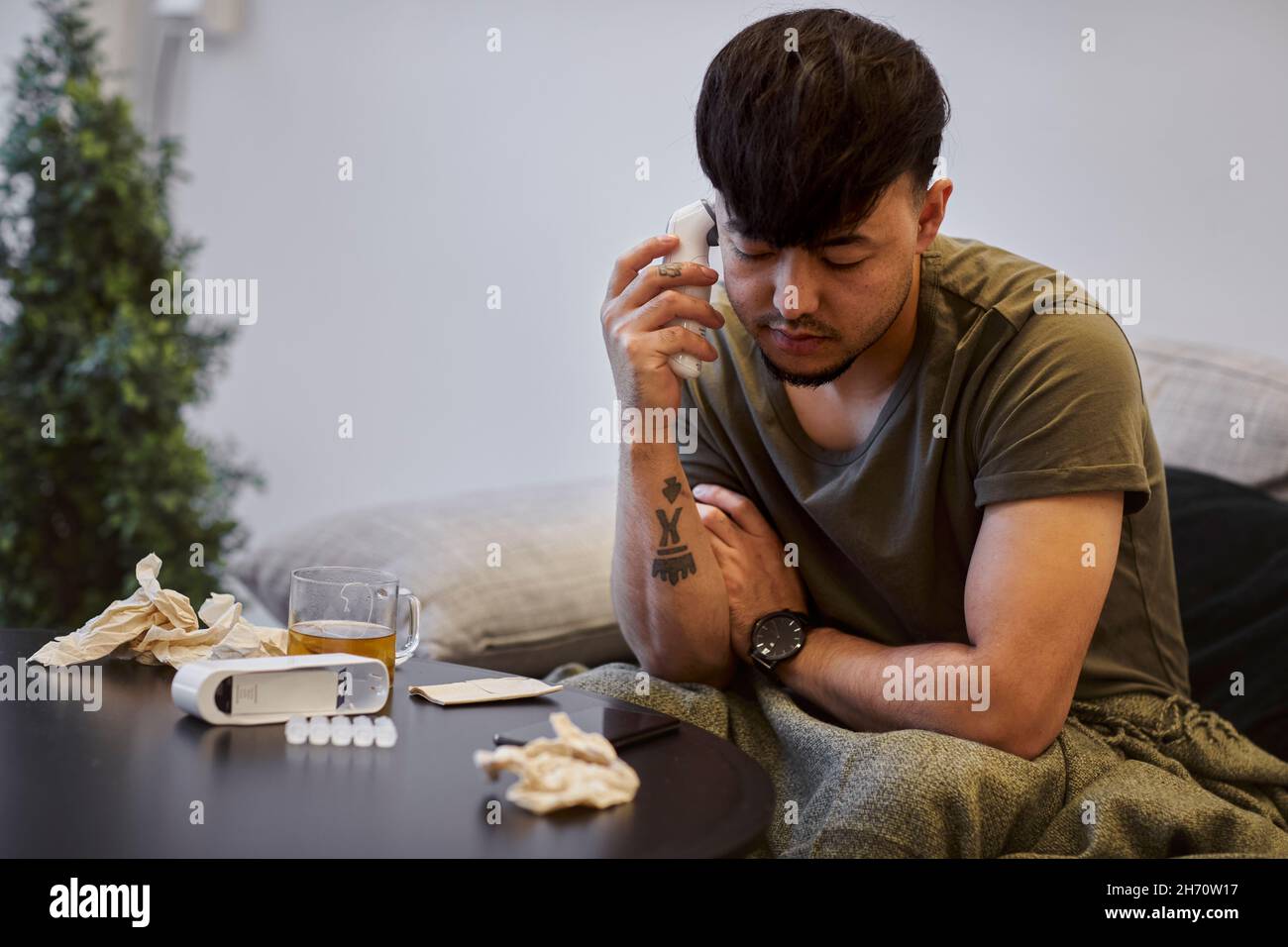 Uomo malato sul divano usando il telefono cellulare Foto Stock