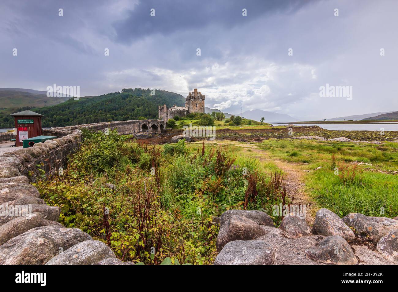 Paesaggio con il Castello di Eilean Donan in Scozia su un'isola. Storico ponte pedonale in pietra conduce al castello. Colline e lago sullo sfondo. Pietra wa Foto Stock