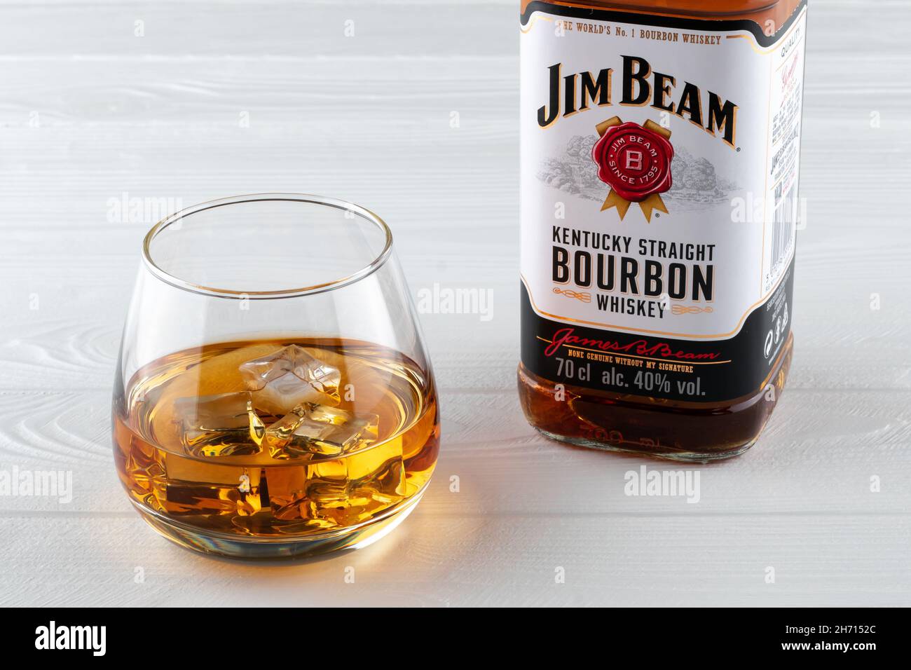 Bottiglia di Jim Beam su un tavolo di legno bianco. Un bicchiere di borbone con ghiaccio. Bevanda forte. Vecchia marca di whiskey. Editoriale illustrativo Foto Stock