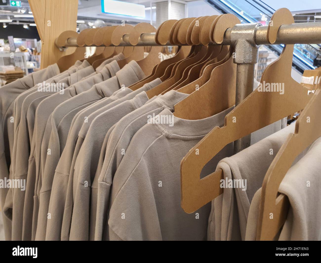 I vestiti in colori naturali trendy appendono su appendiabiti di carta di cartone eco-friendly su scaffale in negozio di vestiti, tonalità pastello. Messa a fuoco selettiva Foto Stock