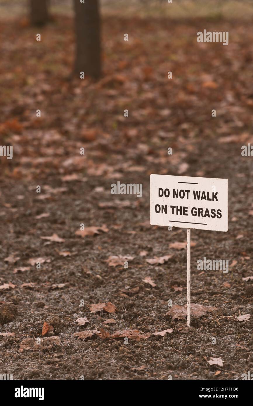 Segno bianco con l'iscrizione in inglese "non camminare sull'erba" su uno sfondo autunno sfocato con alberi e foglie cadute Foto Stock