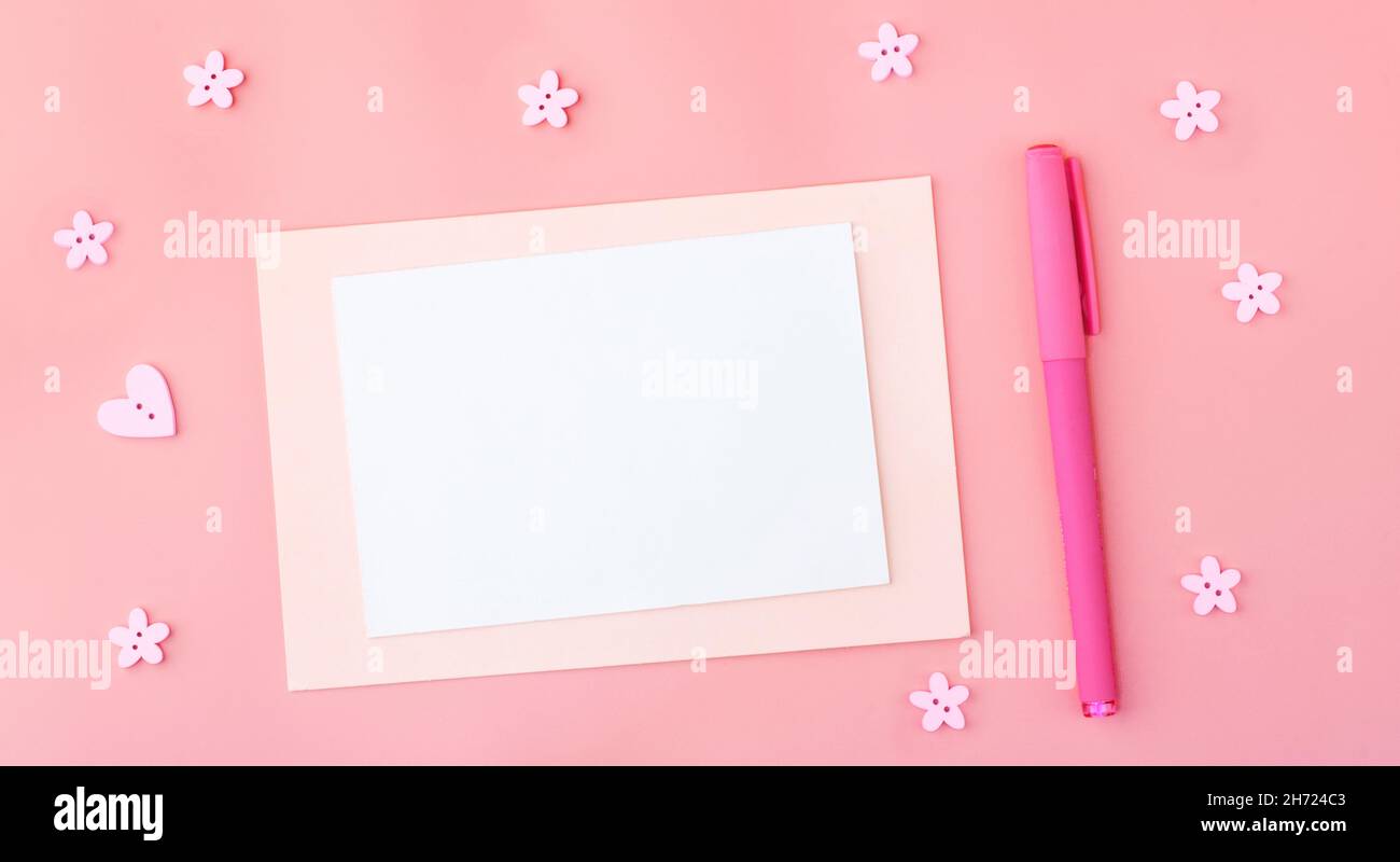 Fogli vuoti colorati di colori pastello su sfondo rosa accanto alla penna, quasi romantici bottoni in forma di fiori e cuori. Spazio di copia Foto Stock