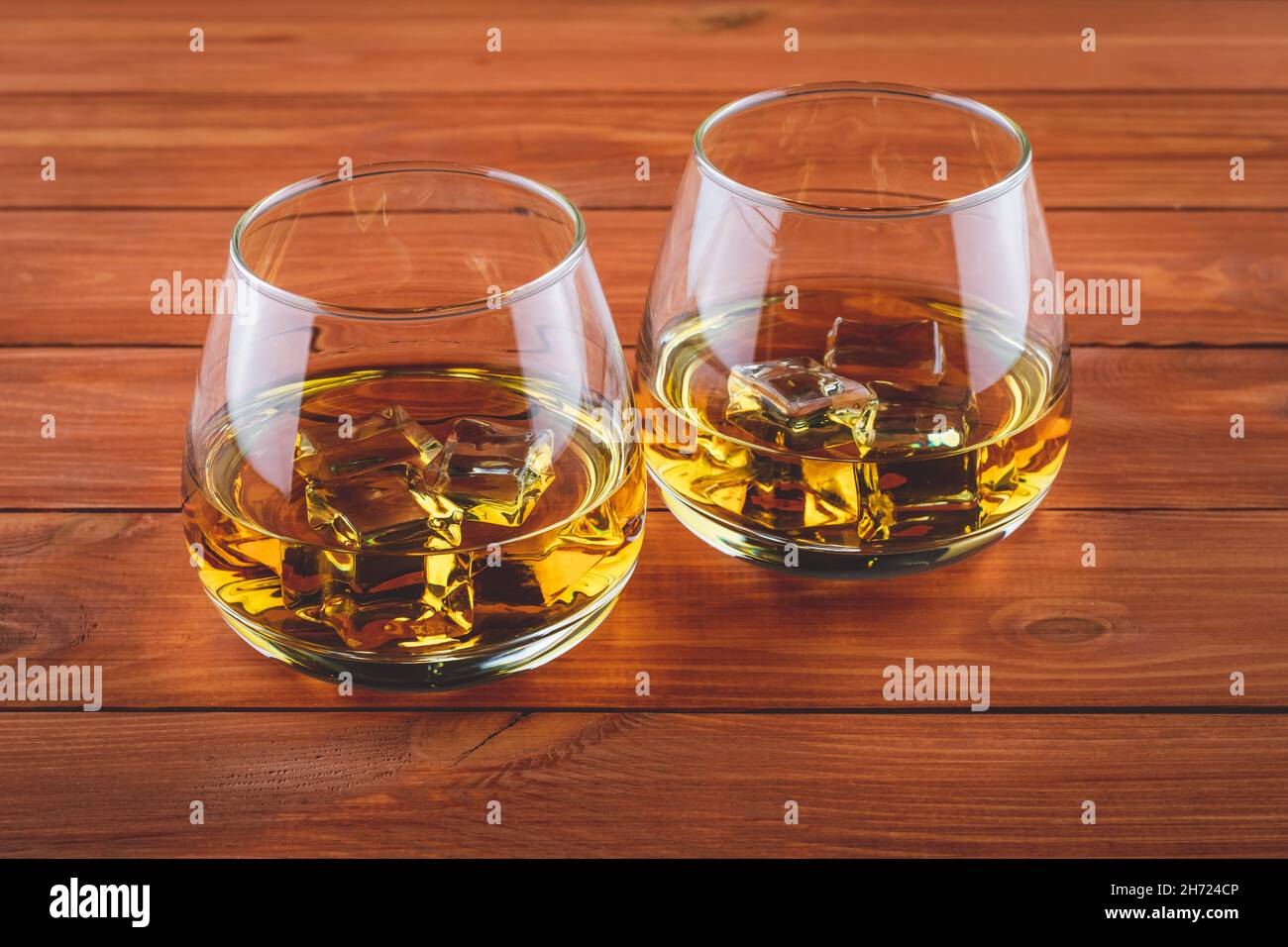 Due bicchieri di whiskey su un tavolo di legno marrone. Un bicchiere di borbone con ghiaccio. Bevanda forte. Vecchio brandy, cognac Foto Stock