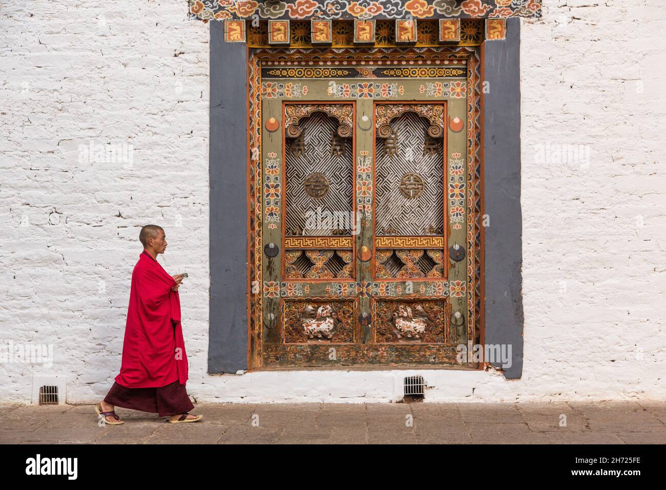 Un monaco buddista passa accanto a una finestra di lavoro in un dochey o cortile nel Punakha Dzong a Punakha, Bhutan. Foto Stock
