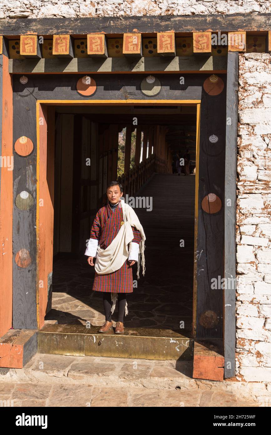 Un giovane uomo bhutanese si trova sulla porta del bazam o ponte coperto per il dzong a Punakha, Bhutan. Foto Stock