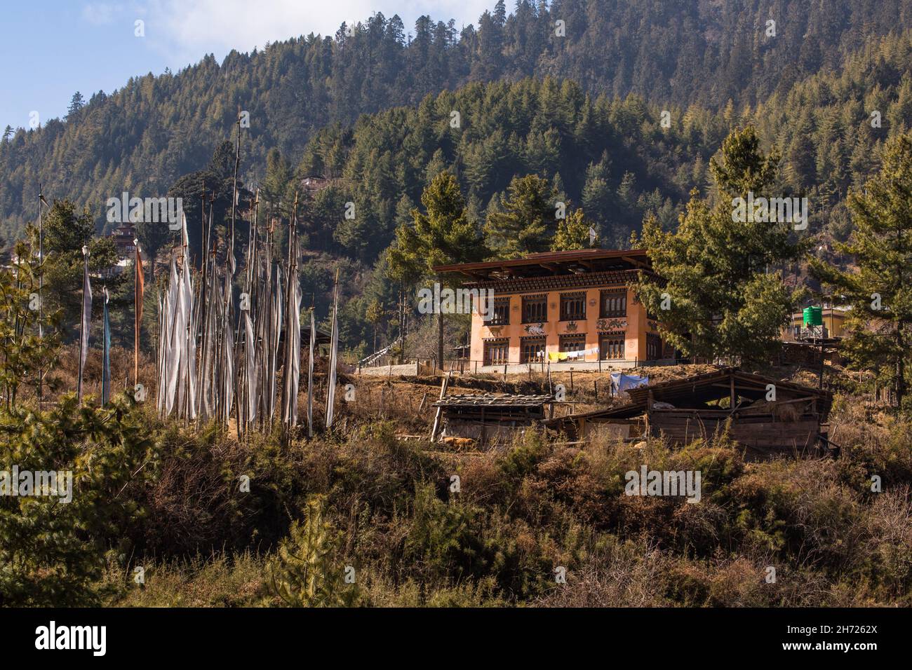 Una tradizionale fattoria bhutanese nel villaggio di Hongtsho, Bhutan. Di fronte vi sono un gruppo di bandiere di preghiera. Foto Stock