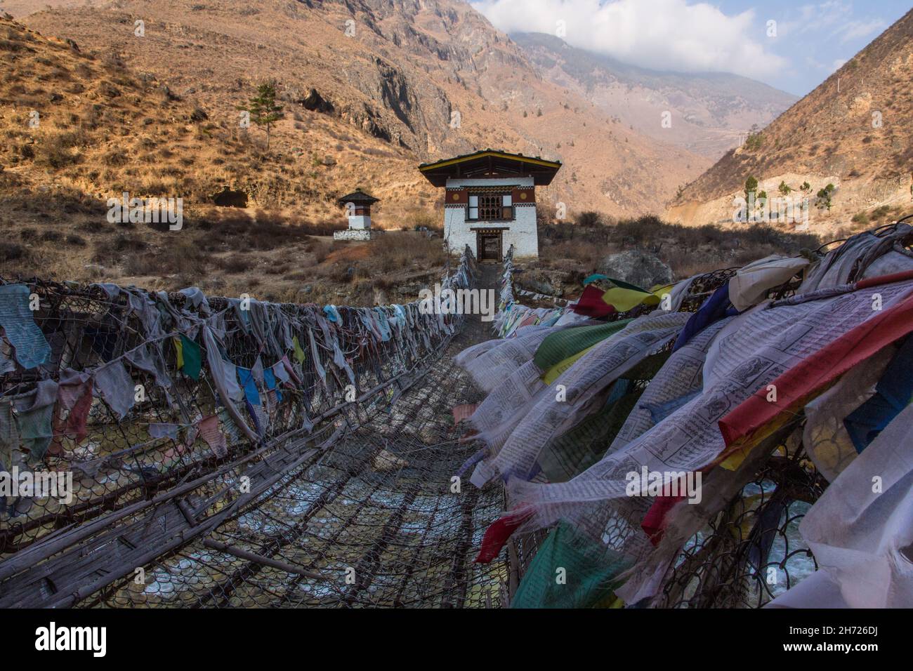 Bandiere di preghiera fiancheggiano il ponte della catena di ferro sul fiume Paro Chhu vicino al tempio di Tamchhog Lakhang in Bhutan. Foto Stock