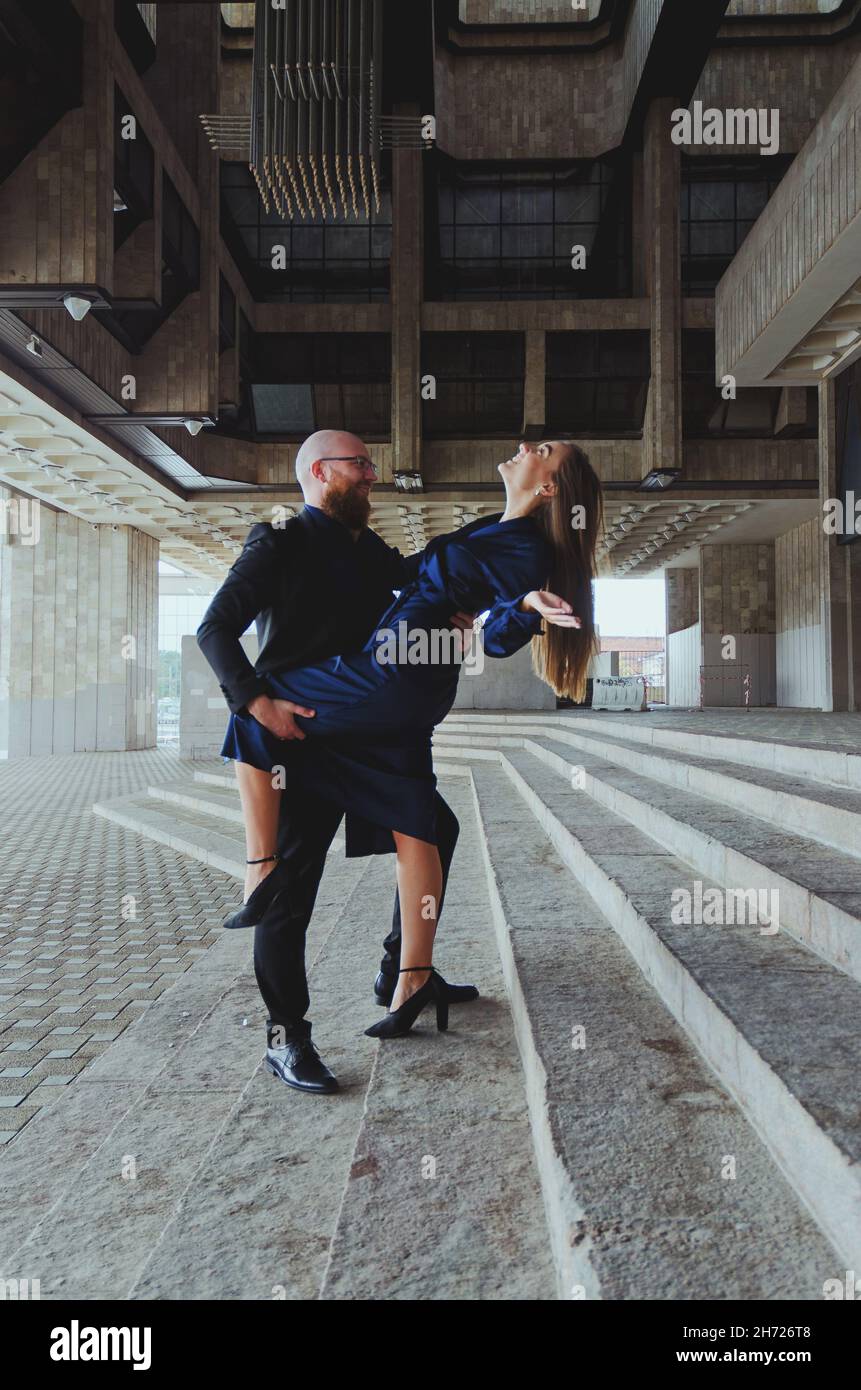 Storia d'amore di coppia elegante: Giovane uomo d'affari in un abito blu con una barba rossa. E una giovane donna carina in abito lungo blu. Vacanza e data in famiglia Foto Stock