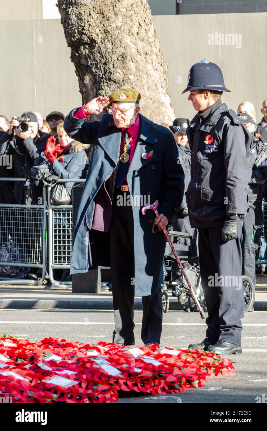 Ufficiale della polizia metropolitana che assiste un veterano anziano a mettere una corona al Cenotaph a Whitehall, Westminster, Londra, Regno Unito, la Domenica della memoria Foto Stock