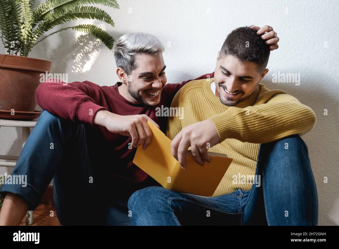 LGBT gay coppia abbraccio e libro di lettura insieme al coperto a casa - omosessuale amore e romanticismo concetto Foto Stock