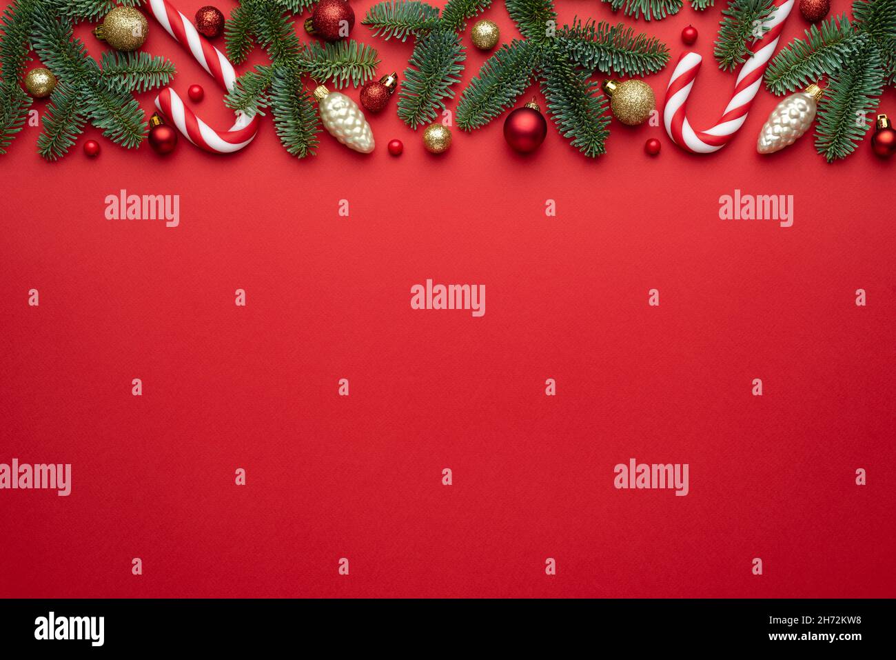 Sfondo rosso natalizio con bordo decorativo in rami di abete e decorazioni ad albero. Disposizione piatta, vista dall'alto e spazio di copia per il testo Foto Stock