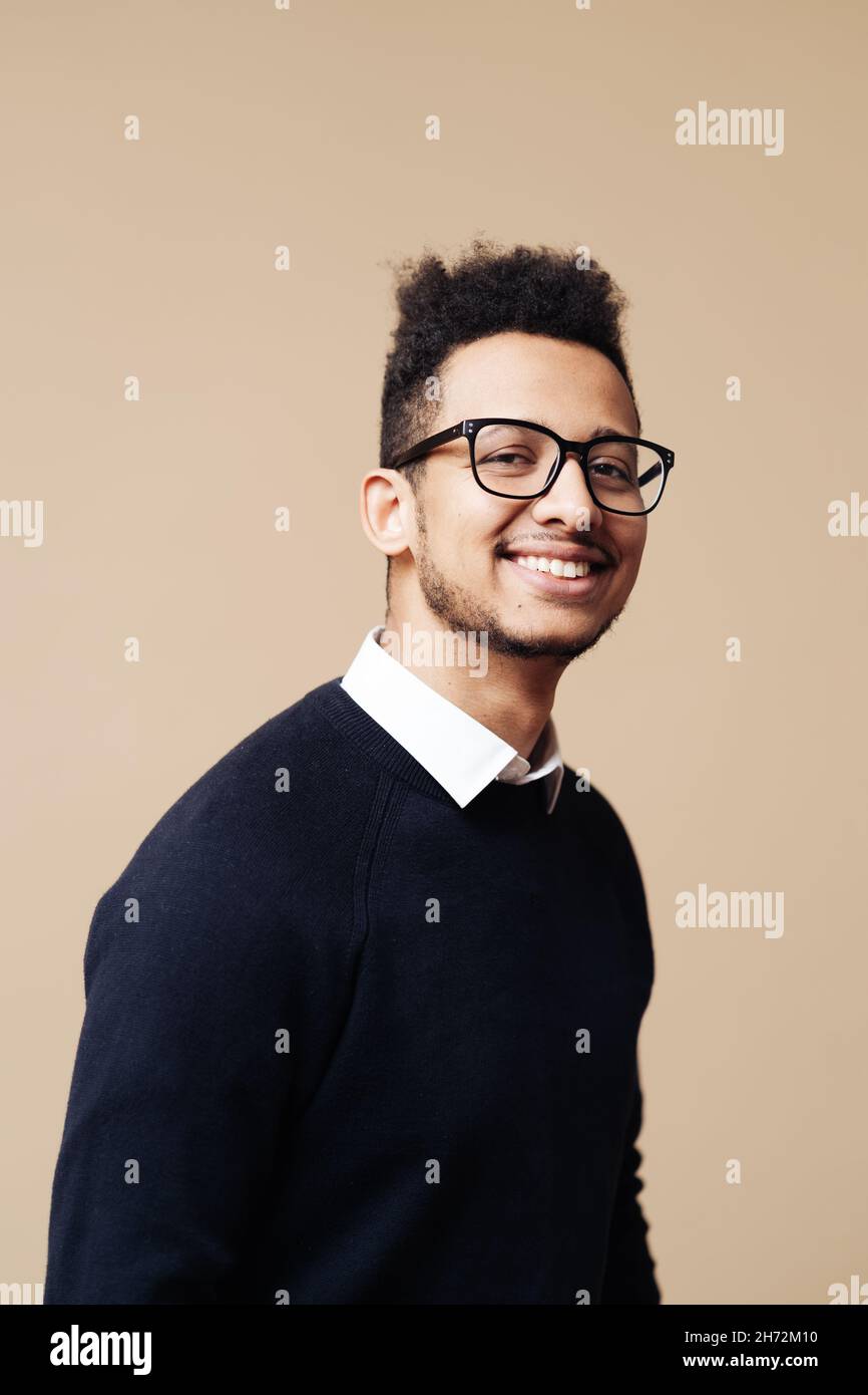Giovane bell'uomo che indossa maglione, camicia bianca e occhiali su sfondo  beige faccia sorridente guardando la fotocamera. Persona positiva, stile  professore Foto stock - Alamy