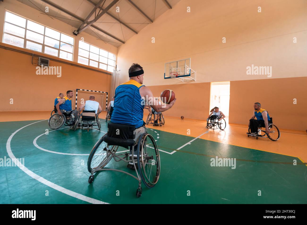 I veterani della guerra disabili hanno mescolato le squadre di pallacanestro di età e di corsa in carrozzina che giocano un match di addestramento in una sala della palestra di sport. Disabili Foto Stock