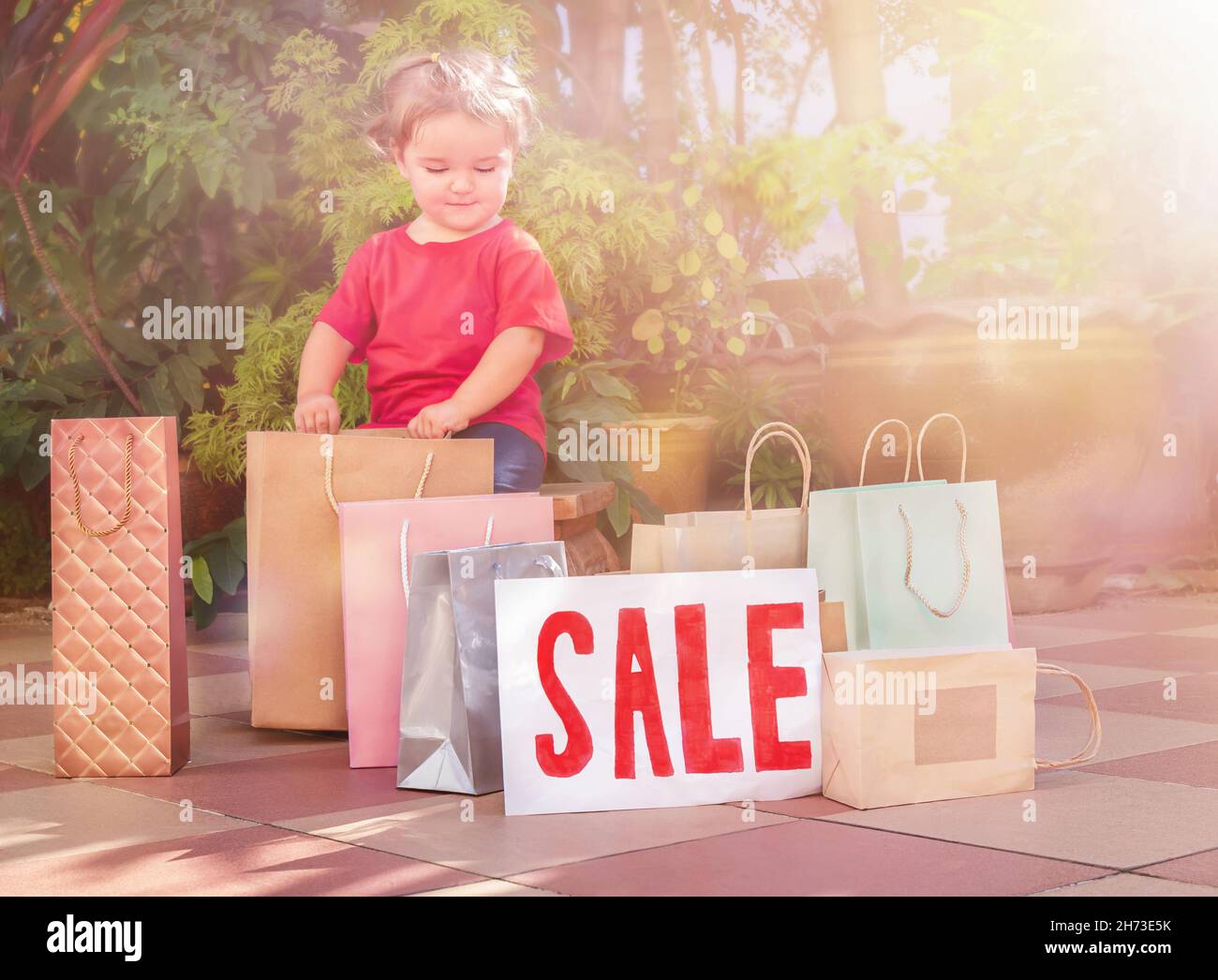 Bambino carino con i sacchetti di shopping e segno di vendita nel cortile posteriore Foto Stock