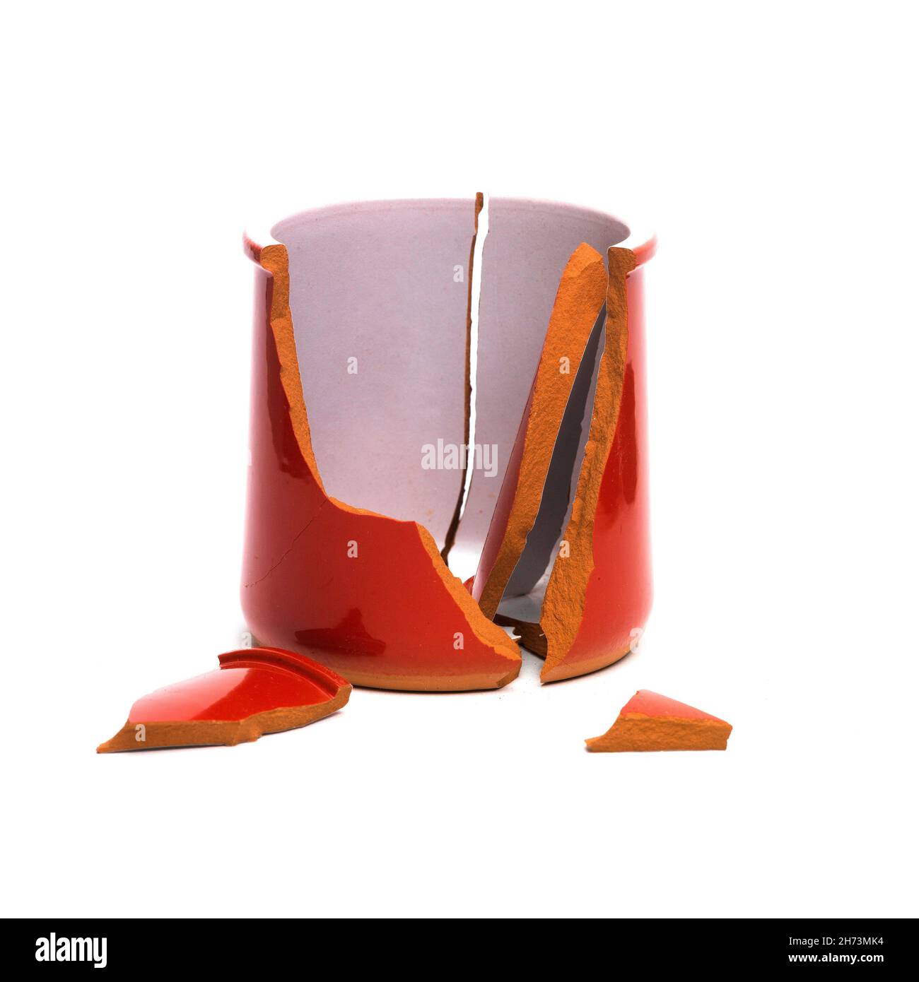 Una pentola di ceramica rossa rotta con pezzi frantumati sparsi su sfondo bianco, che mostra le conseguenze di un incidente Foto Stock