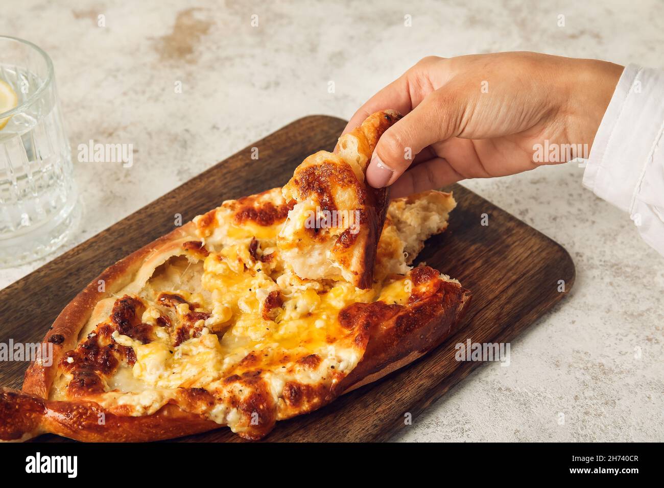 Donna che mangia saporito khachapuri Ajarian da tavola di legno Foto Stock