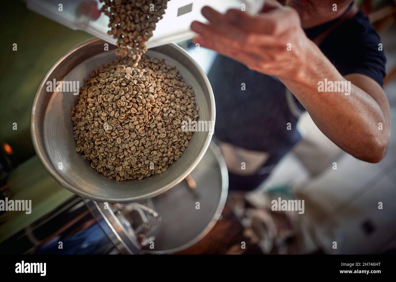 Un uomo versa chicchi di caffè profumati e aromatici nel macinacaffè. Caffè, bevande, produzione Foto Stock