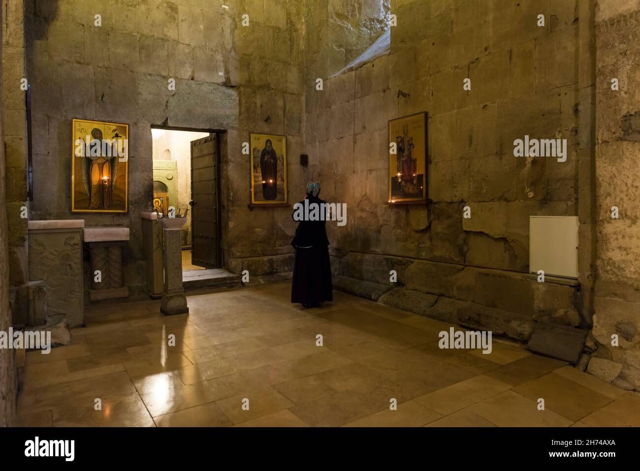 Donna in abiti neri che prega di fronte ad un'icona nella Cattedrale Svetitskhoveli. Provincia di Mtskheta-Mtianeti, Georgia, Caucaso Foto Stock