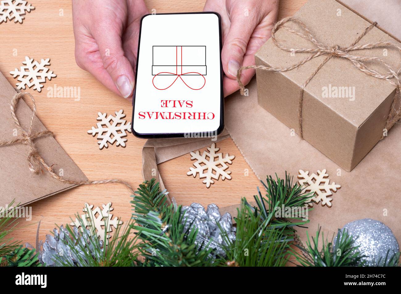 Primo piano mani tenendo un cellulare con uno schermo bianco con la vendita di iscrizione e un regalo disegnato su un tavolo di legno con scatole regalo di Natale, neve Foto Stock