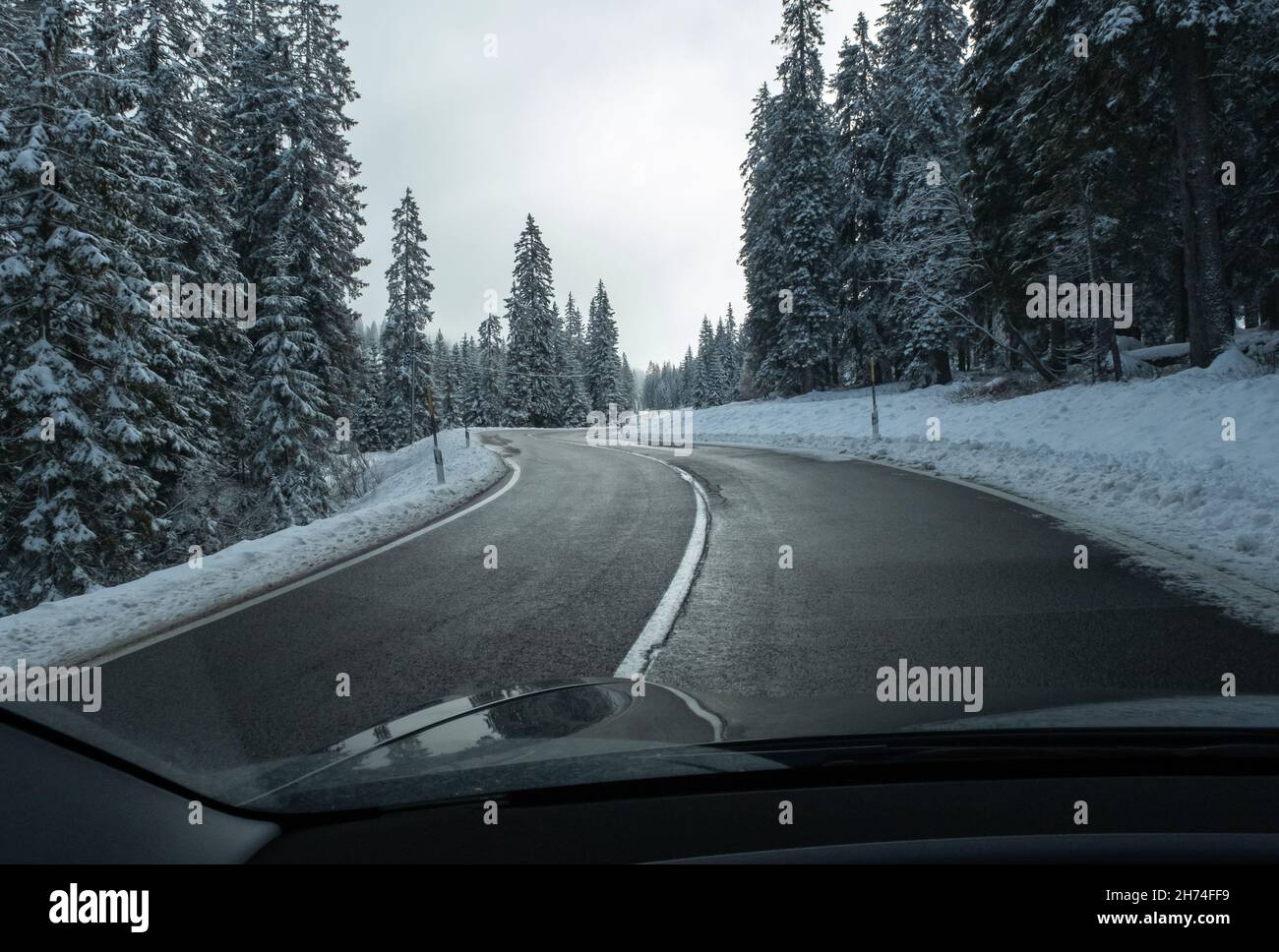 Un colpo in movimento da dietro il parabrezza di un'auto elettrica con montagne innevate delle alpi. Freddo nuvoloso giorno d'autunno. Foto vista POV in prima persona Foto Stock