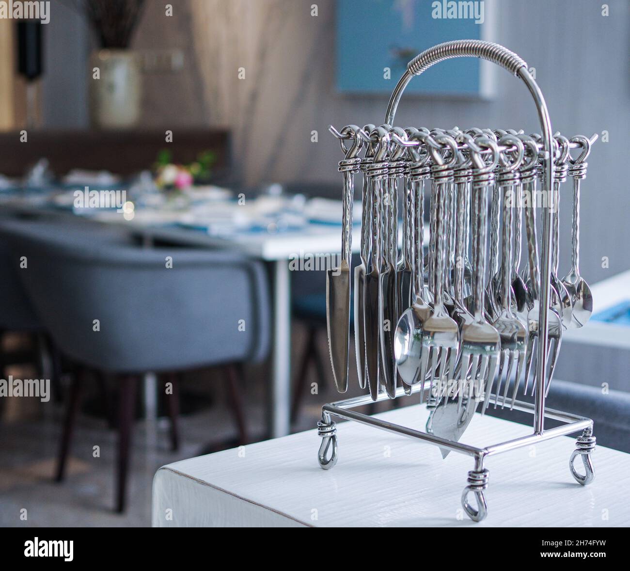 Elegante coltelleria in acciaio inossidabile color argento, posate, cucchiai, forchette, coltelli, appendiabiti, rack su tavolo da ristorante bianco Foto Stock