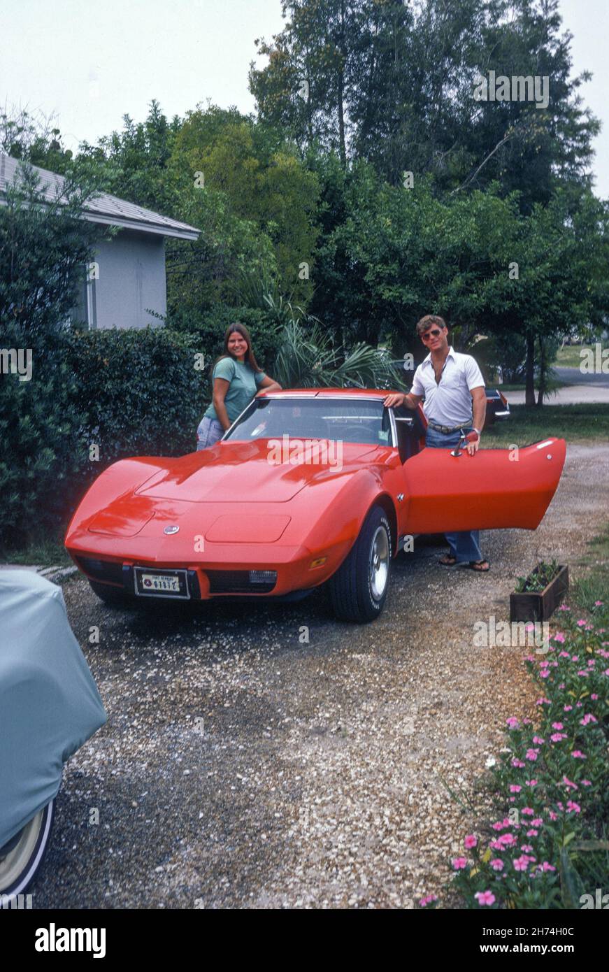 Giovane coppia Stand by a Red 1975 Corvette in un vialetto Subiban, Tampa, FL 1975 Foto Stock